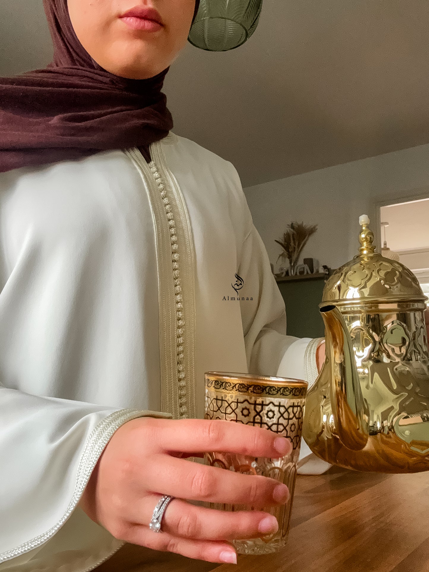 Person holding a glass with a gold teapot in the background
