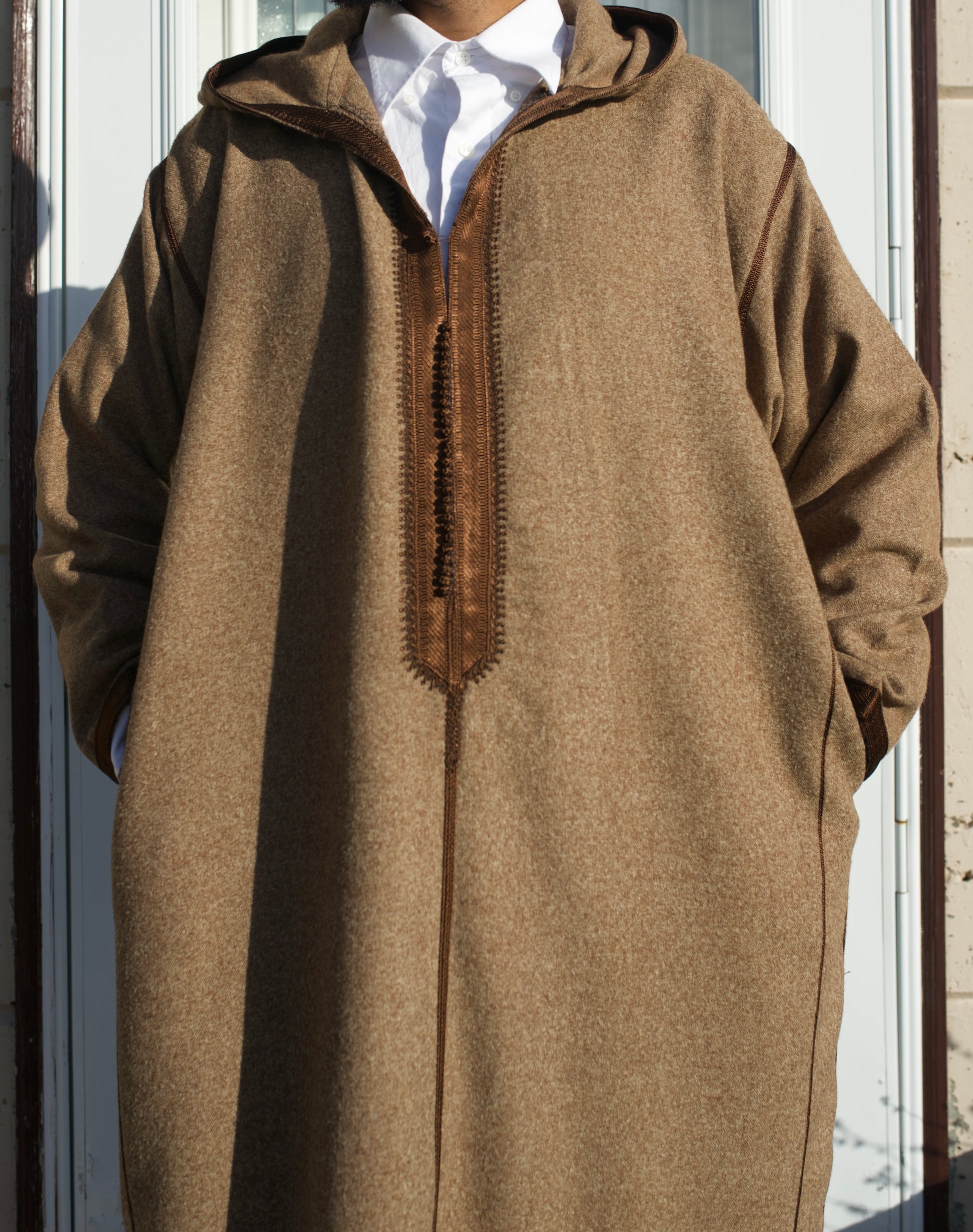 Person wearing a brown hooded garment with a white shirt underneath, standing against a neutral background.