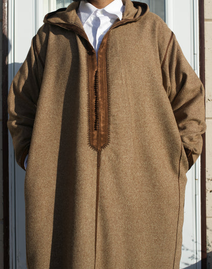 Person wearing a brown hooded garment with a white shirt underneath, standing against a neutral background.