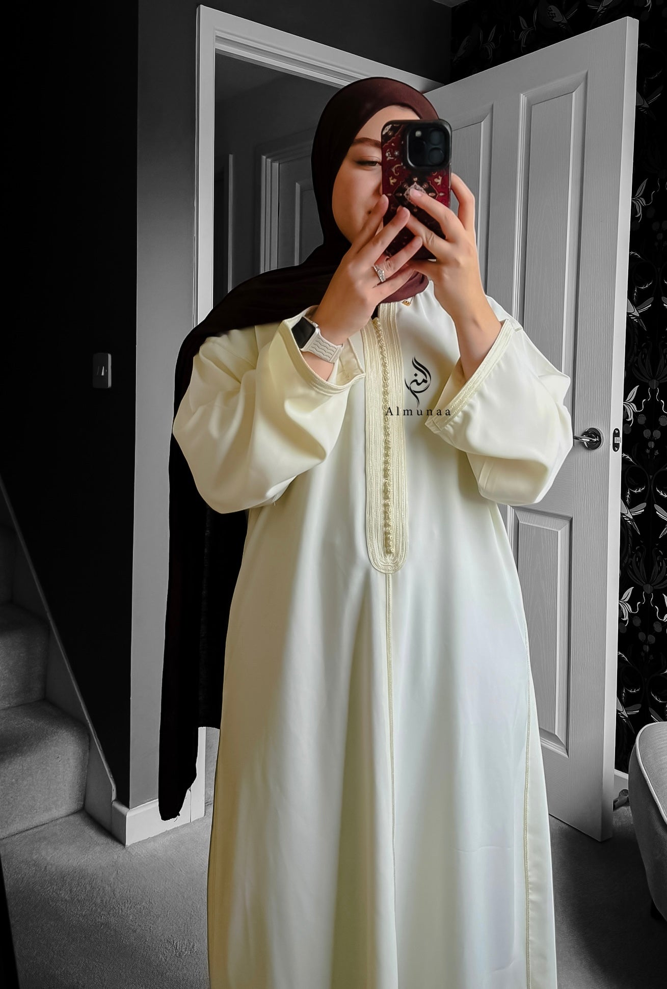 Person wearing a white outfit with a logo, standing in a room with a door and wall.