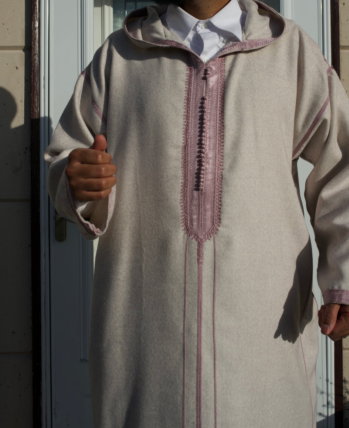 Person wearing a light brown traditional outfit with intricate embroidery, standing against a neutral background.