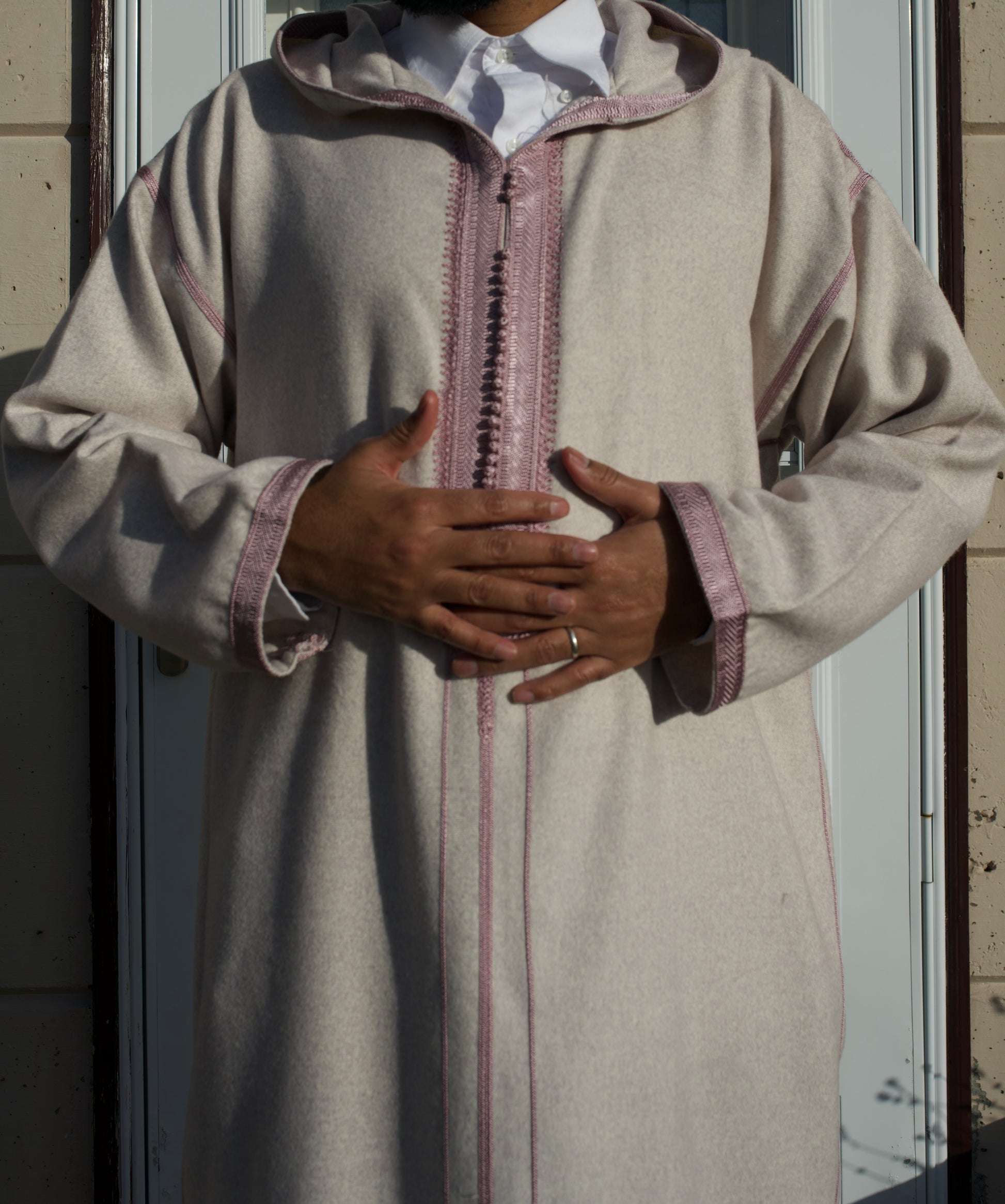 Person wearing a traditional beige robe with pink accents, standing against a neutral background.