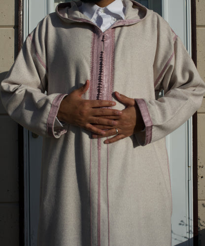 Person wearing a traditional beige robe with pink accents, standing against a neutral background.