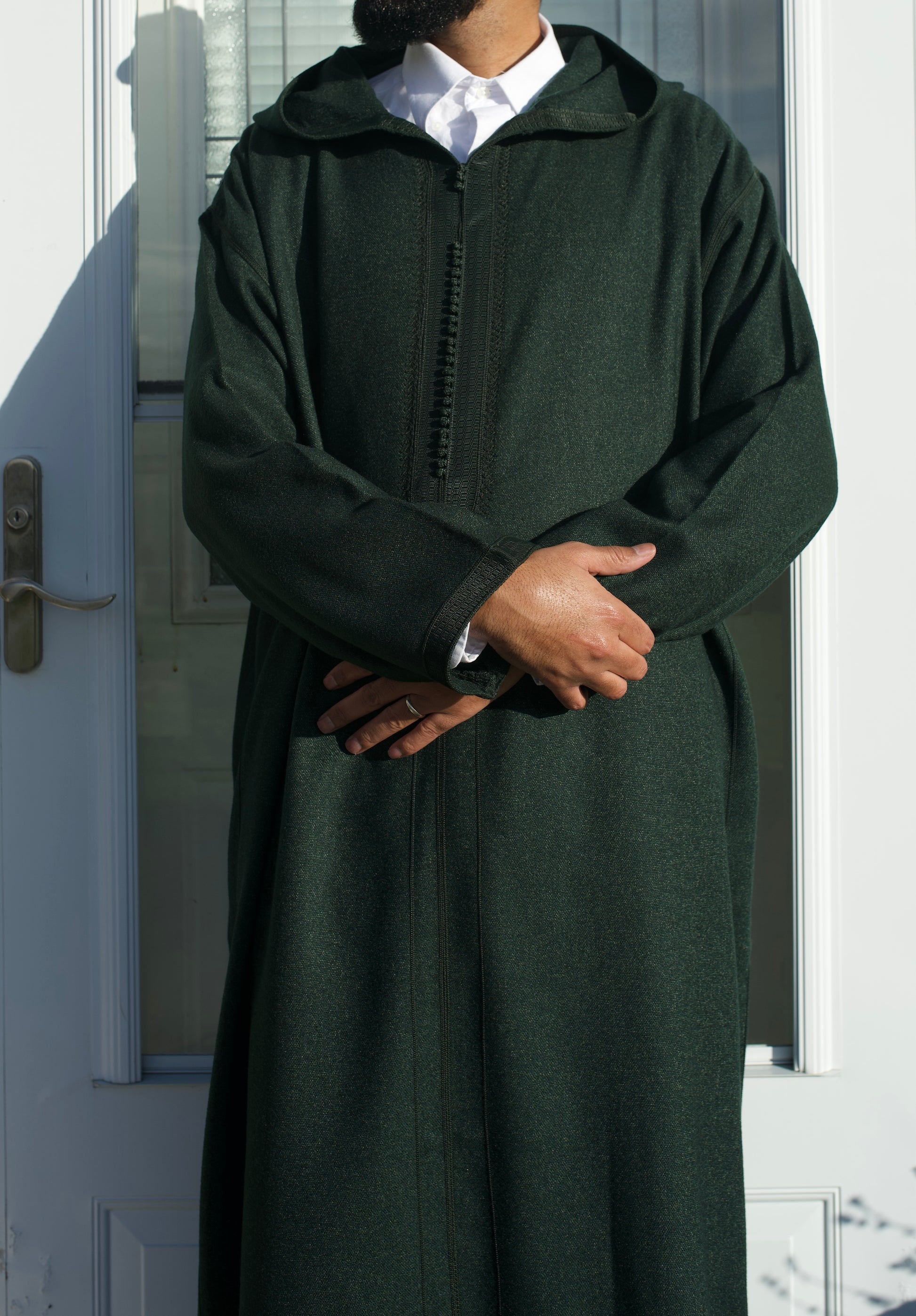 Person wearing a dark green hooded garment in front of a door.