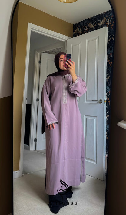 Person wearing a light purple dress with black designs in a room.