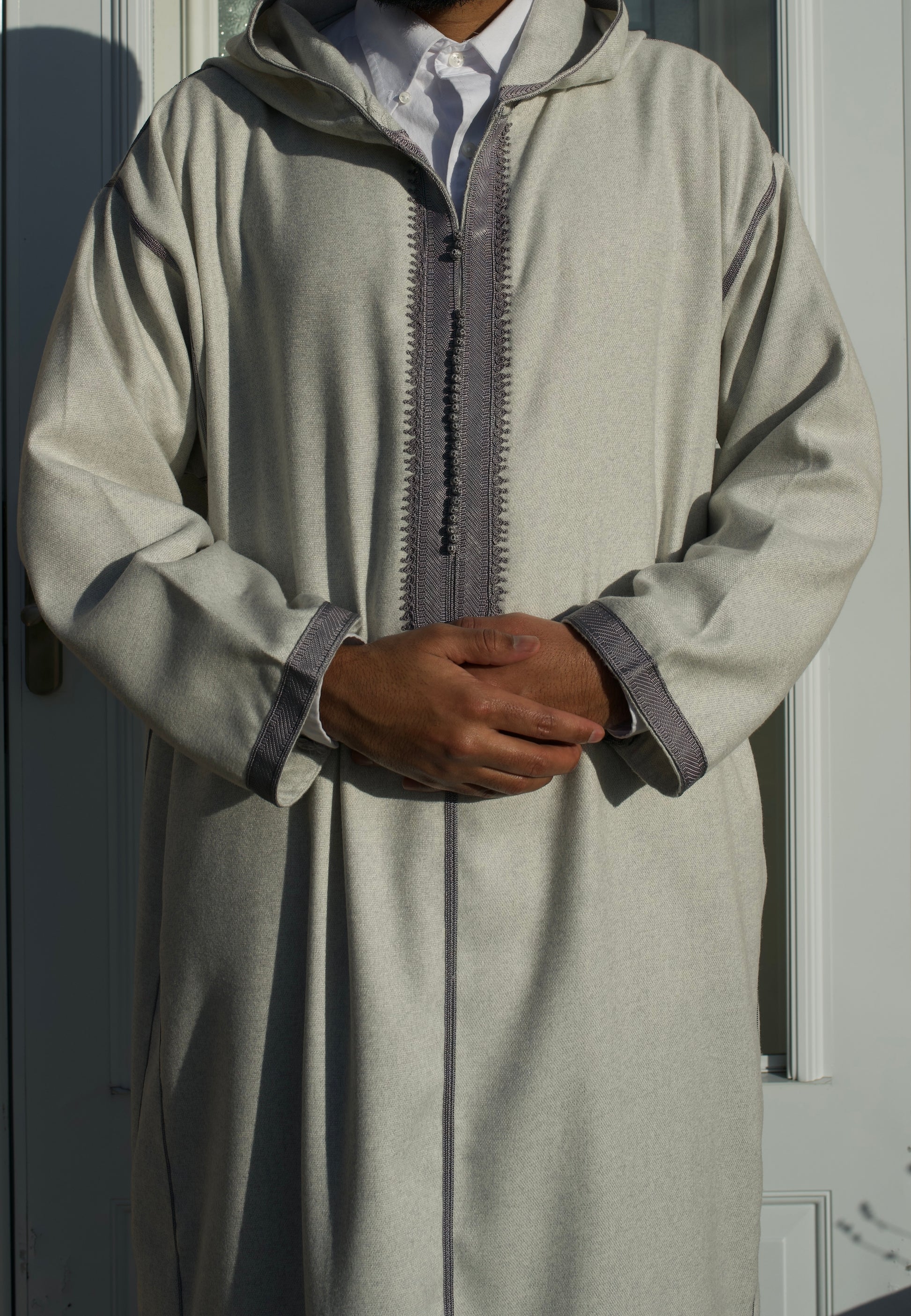Person wearing a light gray traditional outfit with a hood against a neutral background