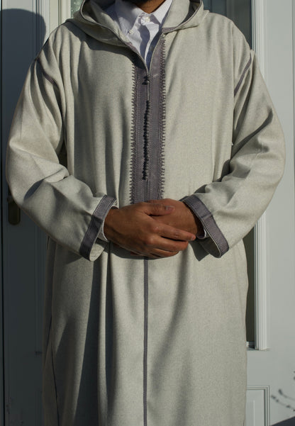 Person wearing a light gray traditional outfit with a hood against a neutral background