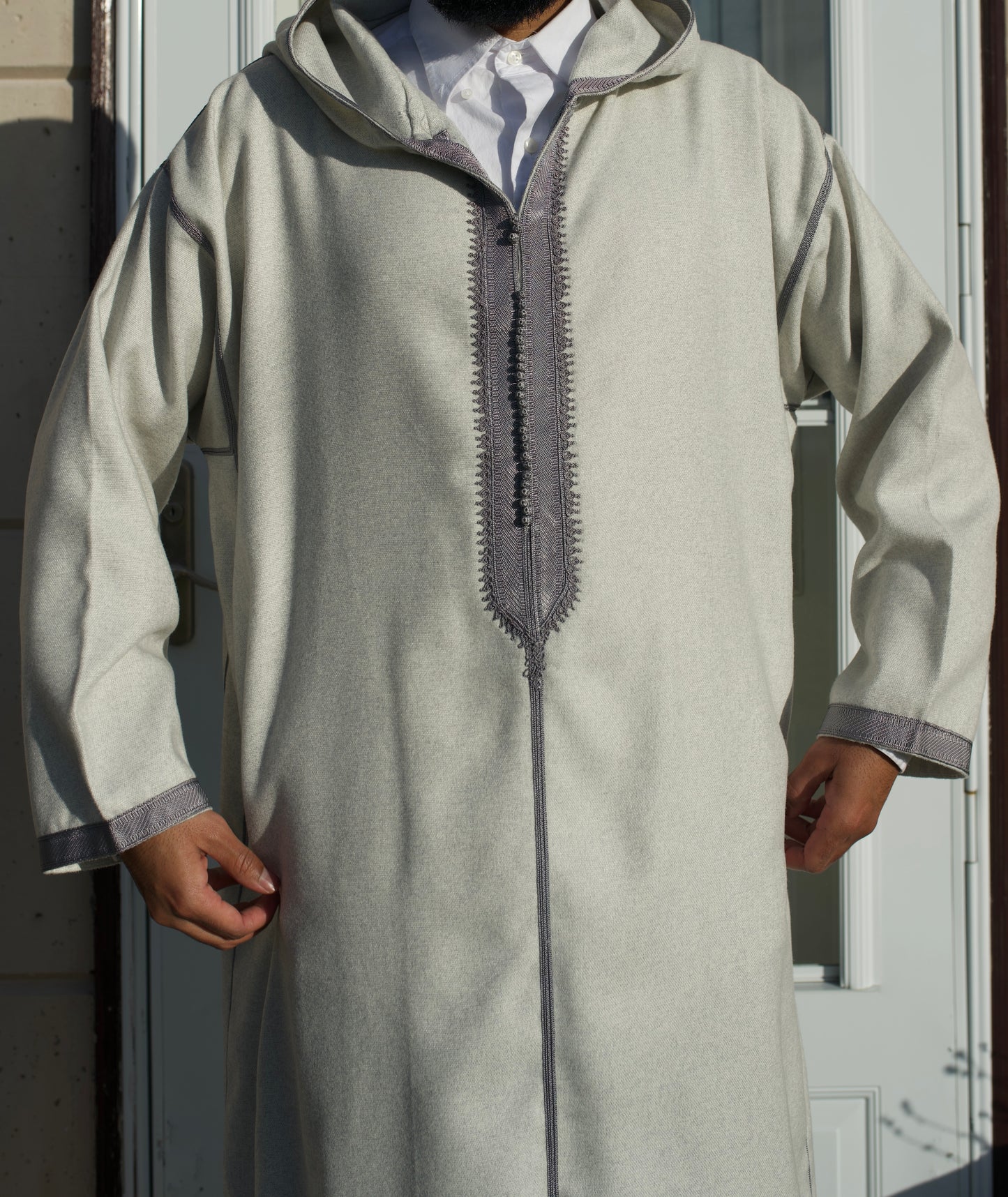 Person wearing a light gray traditional outfit with a hood in front of a door.