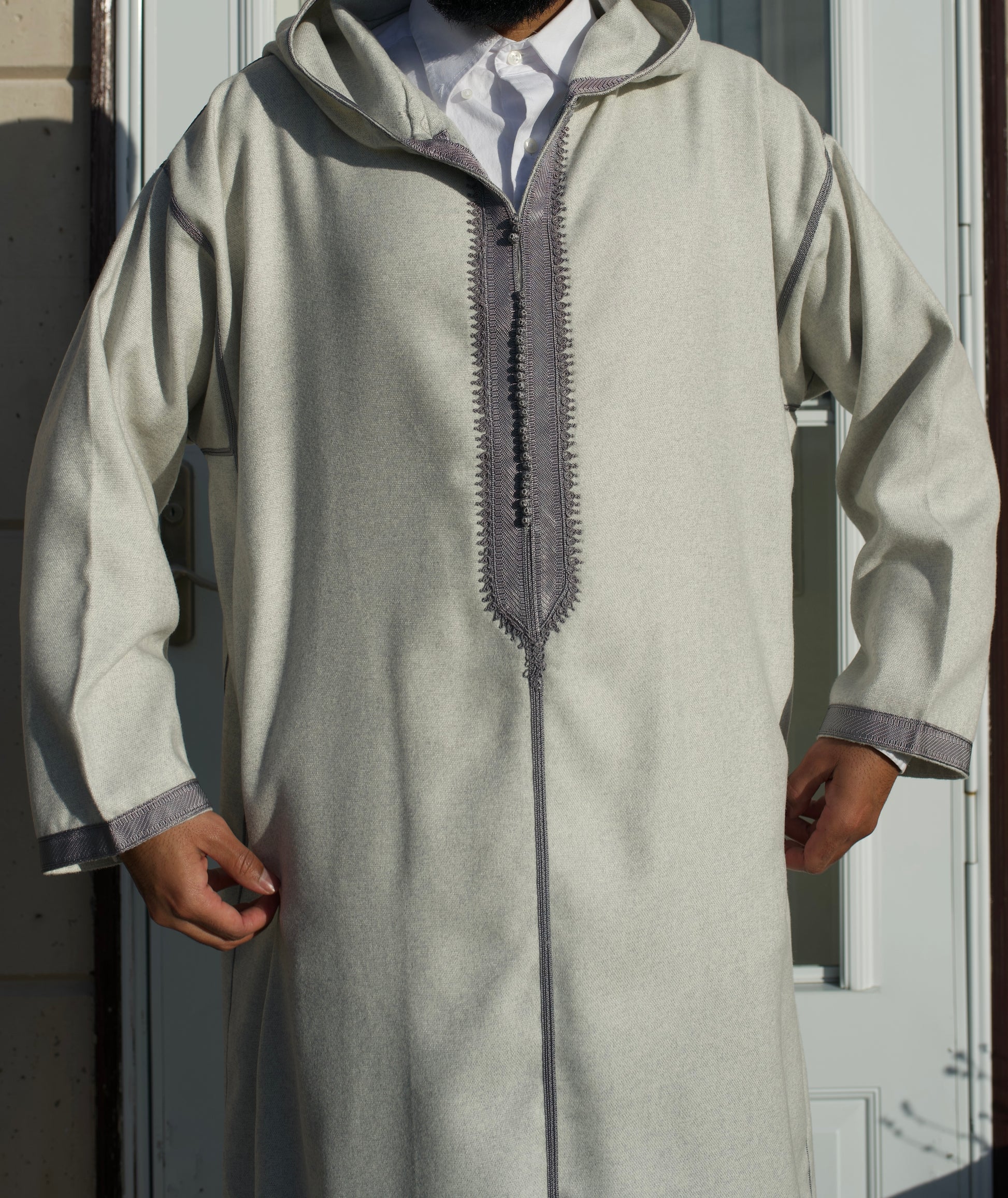 Person wearing a light gray traditional outfit with a hood in front of a door.