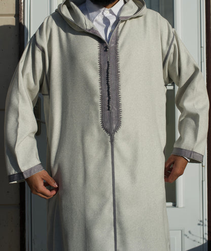 Person wearing a light gray traditional outfit with a hood in front of a door.