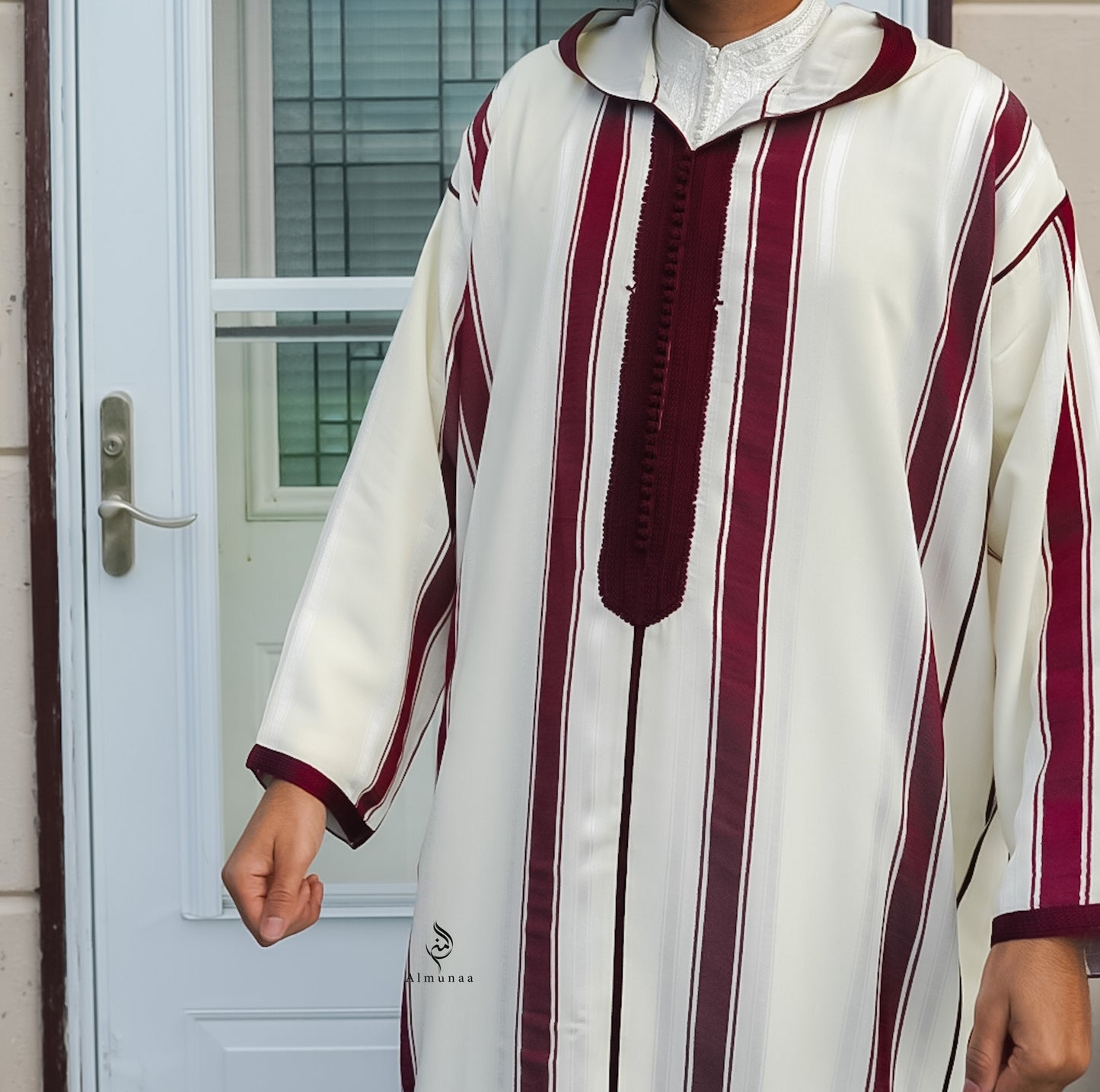 Person wearing a white and maroon striped traditional outfit in front of a door.