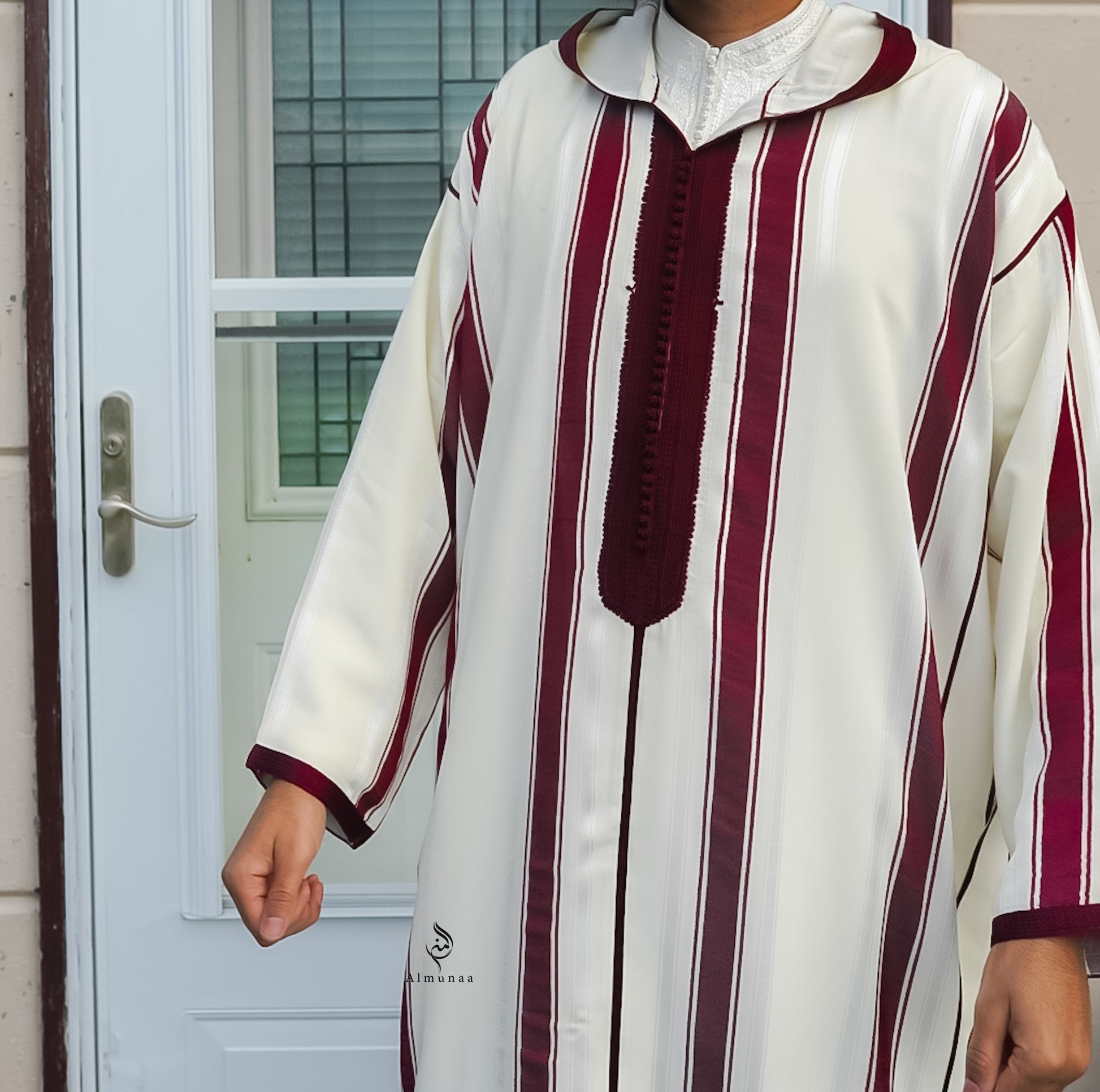 Person wearing a white and maroon striped traditional outfit in front of a door.