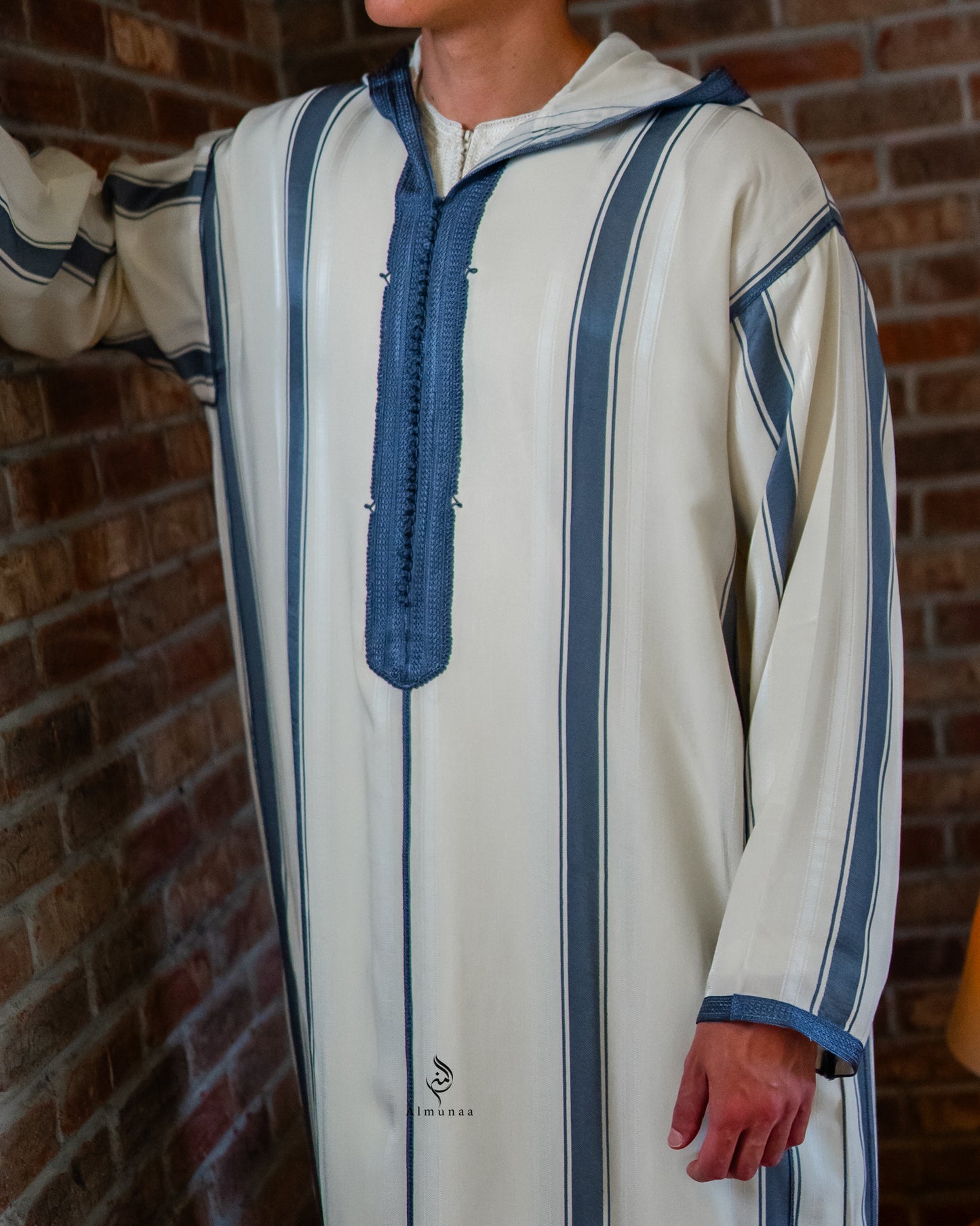 Person wearing a traditional outfit with blue and white stripes against a brick wall.