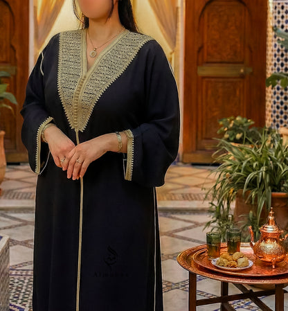 Person wearing a black abaya with gold embroidery in a decorated room.