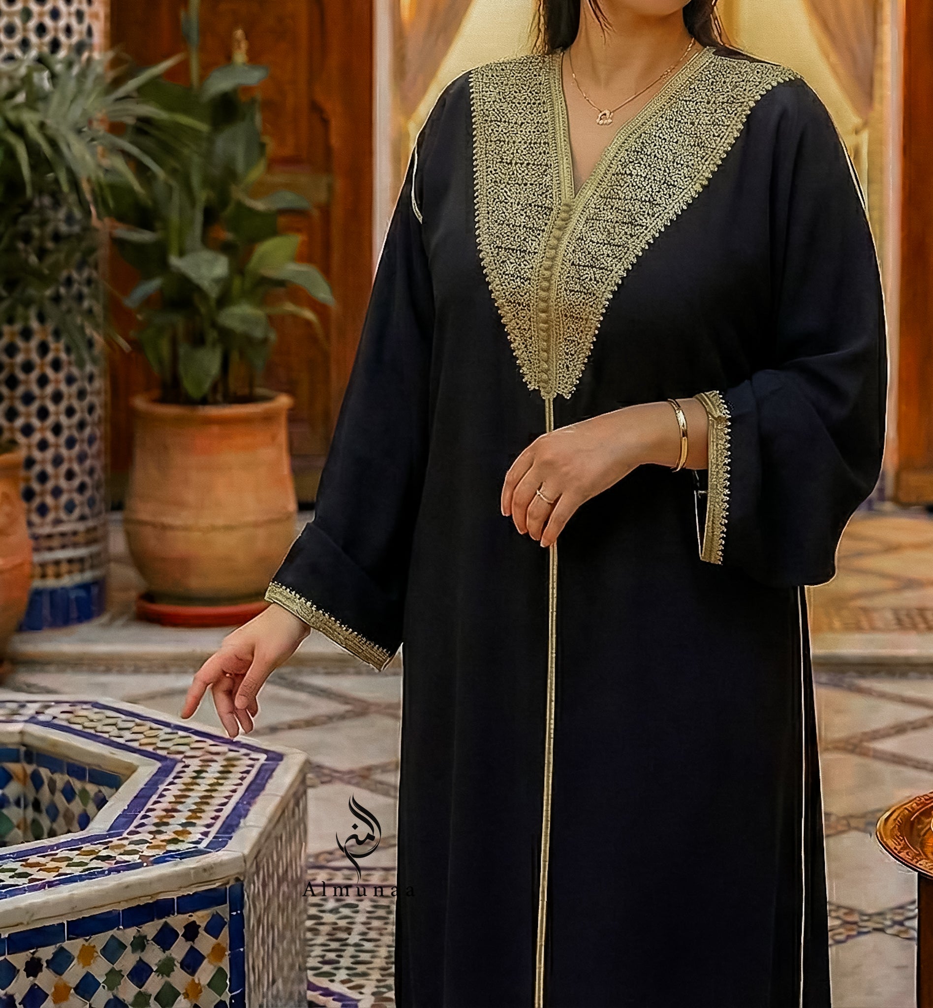 Person wearing a black abaya with gold embroidery in a decorative indoor setting.