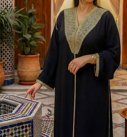 Person wearing a black abaya with gold embroidery in a decorative indoor setting.