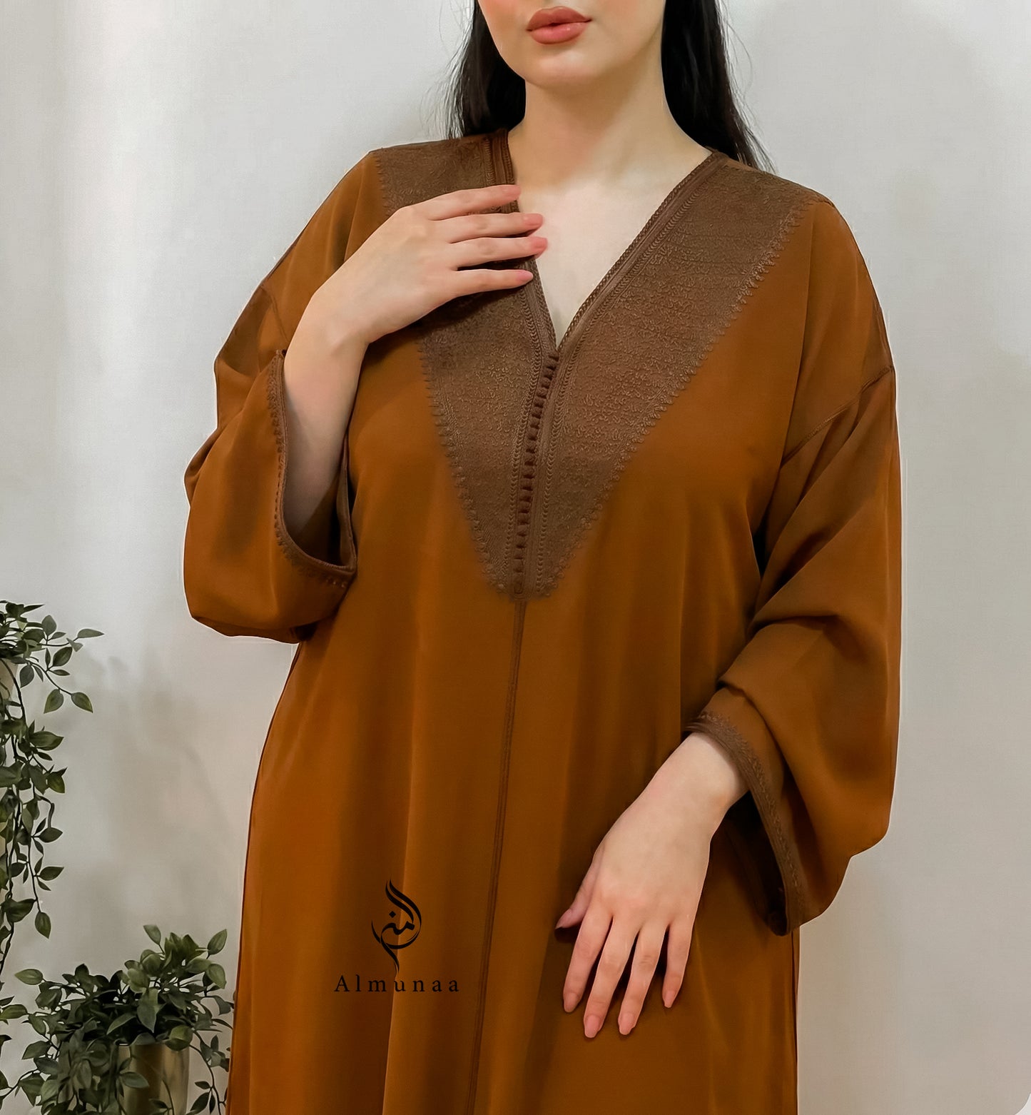 Brown dress with a V-neckline worn by a person, with 'Almunaa' branding visible.